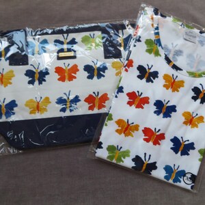 May include: A white tote bag and a white t-shirt, both with a repeating pattern of colorful butterflies in orange, yellow, blue, and green. The tote bag has a navy blue trim.