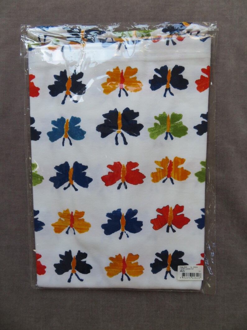 May include: White fabric with a repeating pattern of colorful butterflies in shades of blue, orange, red, and green. The butterflies have a simple, stylized design. The fabric is packaged in a clear plastic bag.