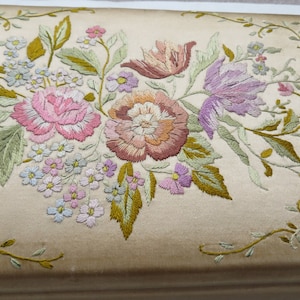 May include: A vintage embroidered floral design on a cream-colored fabric. The design features pink, purple, and peach flowers with green leaves.