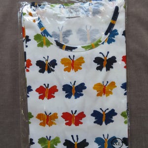 May include: White t-shirt with a colorful butterfly pattern. The butterflies are in various colors, including red, orange, blue, green, and black. The shirt is folded and sealed in a clear plastic bag. The shirt has a round neckline.