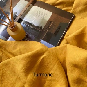 May include: A close-up of a yellow linen fabric with the word "Turmeric" printed on it. The fabric is textured and has a natural, rustic look.