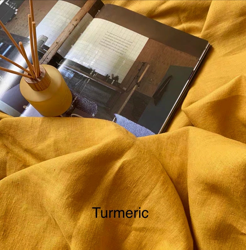 May include: A close-up of a yellow linen fabric with the word "Turmeric" printed on it. The fabric is textured and has a natural, rustic look.