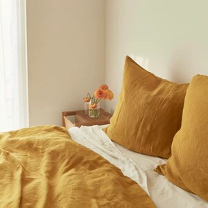 May include: A mustard yellow linen duvet cover and two matching pillowcases on a bed with white sheets.