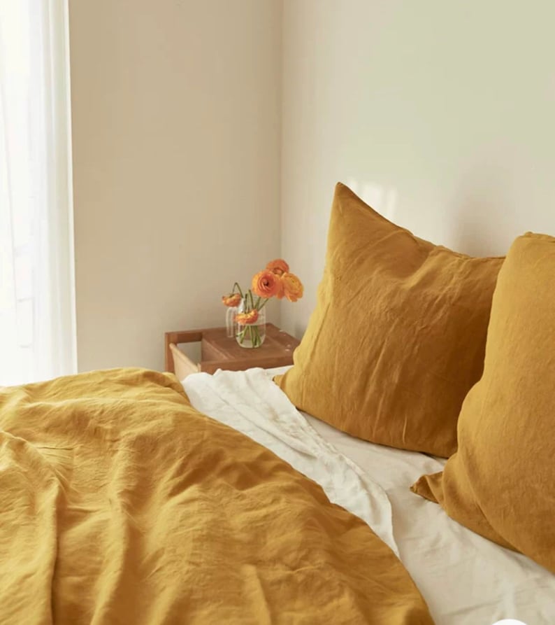 May include: A mustard yellow linen duvet cover and two matching pillowcases on a bed with white sheets.