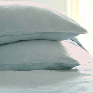 May include: Two light blue linen pillowcases stacked on top of each other. The pillowcases are made of a soft, natural fabric and have a slightly textured surface.