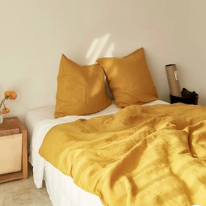 May include: A bed with a yellow linen duvet cover and two matching pillowcases. The bed is made with white sheets and has a white bed skirt.