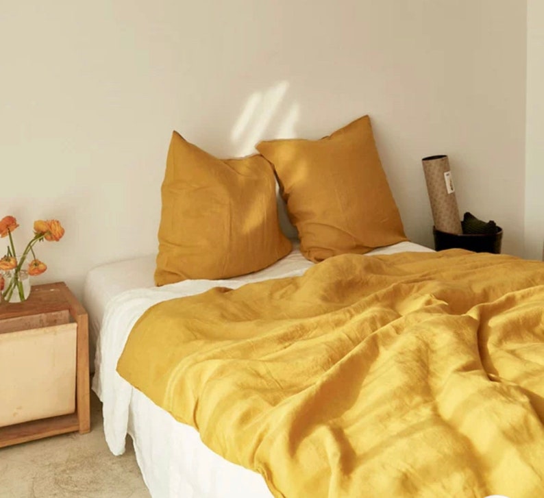 May include: A bed with a yellow linen duvet cover and two matching pillowcases. The bed is made with white sheets and has a white bed skirt.