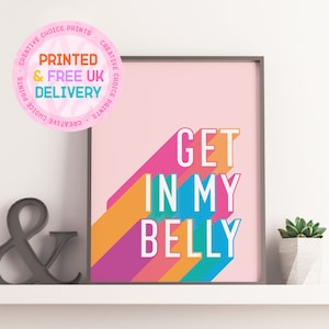 Pode incluir: Um fundo rosa com listras coloridas e o texto "GET IN MY BELLY" em letras brancas. A impressão está emoldurada em uma moldura preta e está sentada em uma prateleira branca.