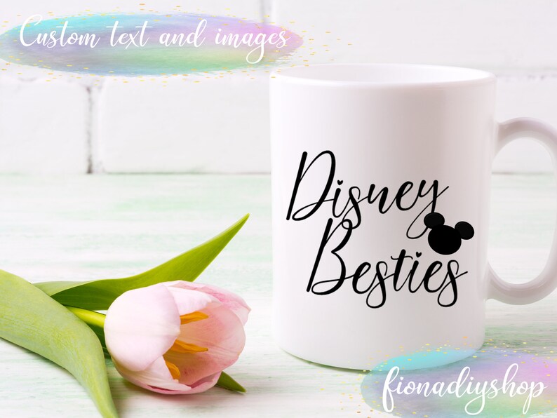 Pu&ograve; includere: Una tazza in ceramica bianca con testo nero che recita "Disney Besties" e una silhouette nera della testa di Topolino. La tazza &egrave; su una superficie di legno bianco con un tulipano rosa.