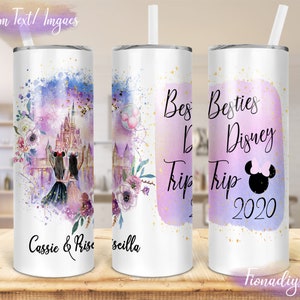 May include: A white tumbler with a lid and straw, featuring a design with a Disney castle, fireworks, and floral accents in purple and blue. Text includes "Besties Disney Trip 2020" and names. The tumbler is on a wooden surface.