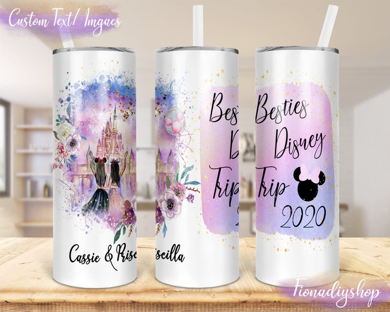 May include: A white tumbler with a lid and straw, featuring a design with a Disney castle, fireworks, and floral accents in purple and blue. Text includes "Besties Disney Trip 2020" and names. The tumbler is on a wooden surface.
