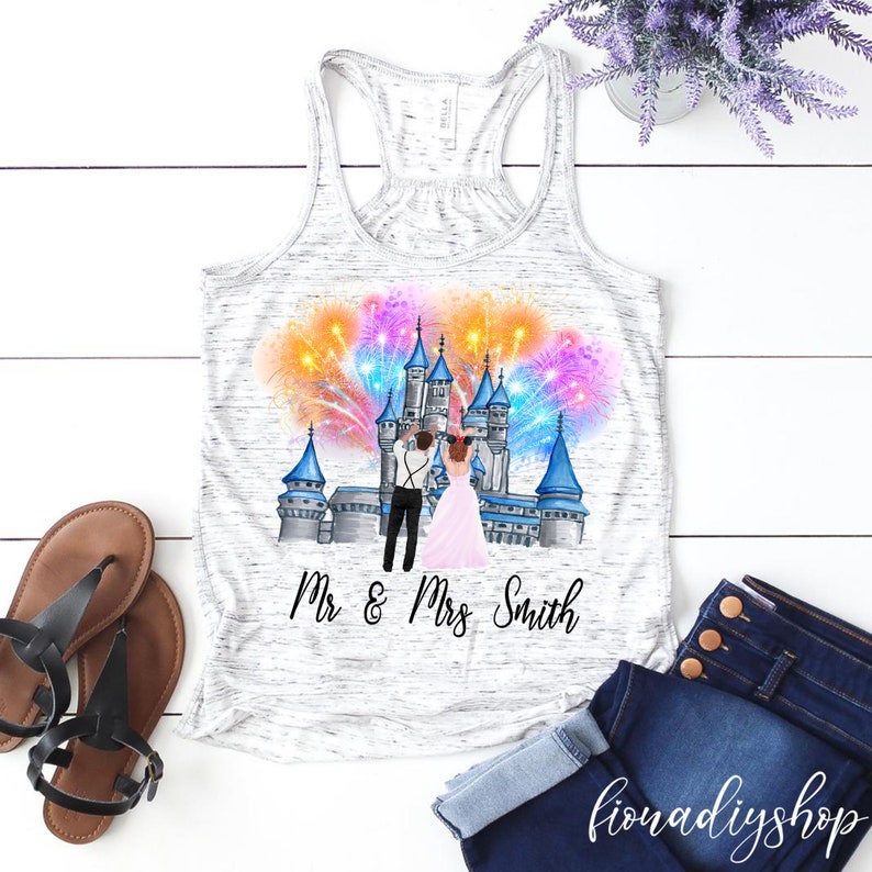 May include: A white tank top with a graphic of a couple in front of a castle with fireworks. The text "Mr & Mrs Smith" is printed below the graphic.