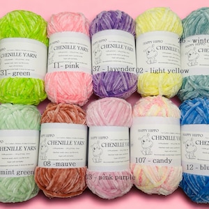 Op de afbeelding: Assortiment van chenille garenklossen in verschillende kleuren, waaronder groen, roze, lavendel, geel, mintgroen, mauve, roze paars, snoep en blauw. Elke klos heeft een label met het Happy Hippo-logo en de kleurnaam.