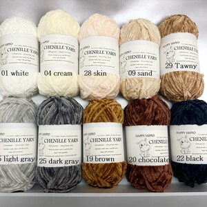 Op de afbeelding: Tien spoelen chenille garen in verschillende kleuren, waaronder wit, cr&egrave;me, huid, zand, bruin, lichtgrijs, donkergrijs, bruin, chocolade en zwart. Elke spoel heeft een label met de merknaam "Happy Hippo" en het kleur nummer en de kleur naam.