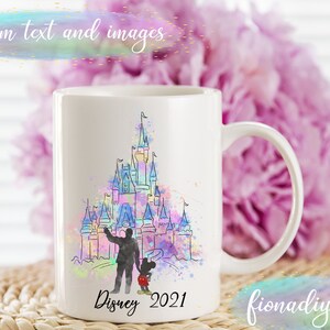 May include: White ceramic mug featuring a watercolor illustration of a castle with a person and Mickey Mouse. The mug has the text "Disney 2021" and "fionadiyshop" printed on it. The background includes a pink flower arrangement.