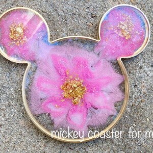 May include: Mickey Mouse-shaped coaster for a mug, featuring a pink floral design with gold leaf accents. The coaster has a gold-colored border and the text "mickey coaster for mug".