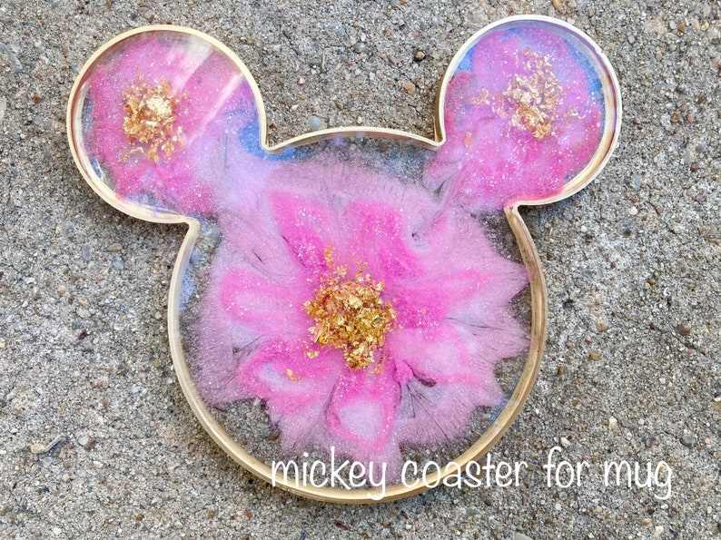 May include: Mickey Mouse-shaped coaster for a mug, featuring a pink floral design with gold leaf accents. The coaster has a gold-colored border and the text "mickey coaster for mug".