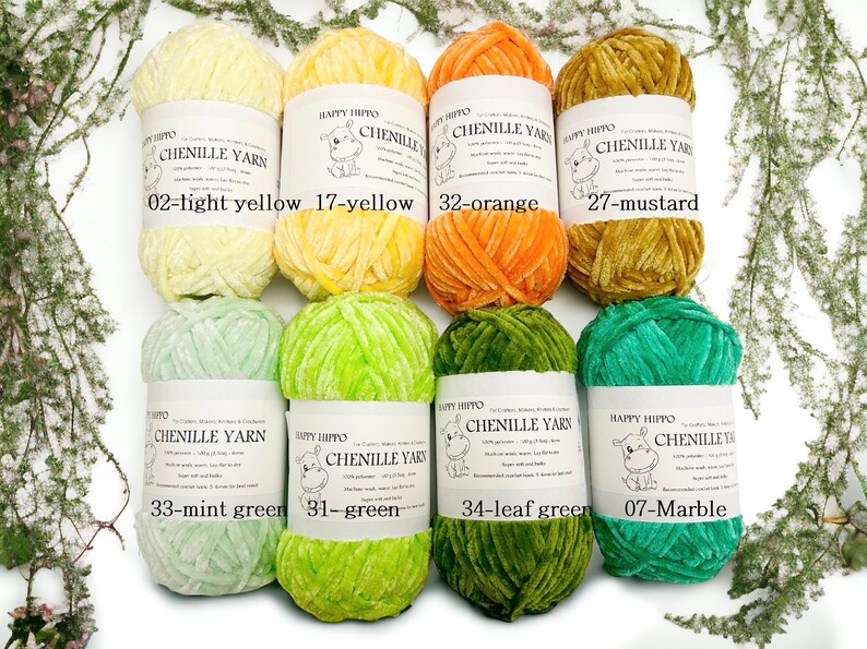 Op de afbeelding: Acht spoelen chenille garen in verschillende kleuren, waaronder lichtgeel, geel, oranje, mosterd, mintgroen, groen, bladeren groen en marmer. Elke spoel heeft een label met de merknaam "Happy Hippo" en de kleurnaam.