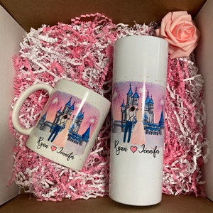 May include: A white mug and a white tumbler with a pink and blue castle illustration and the text "Ryan Jennifer" with a heart symbol between the names. The mug and tumbler are in a white box with pink and white shredded paper.