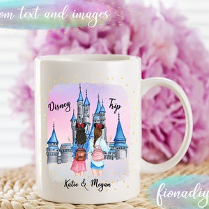 Pu&ograve; includere: Tazza in ceramica bianca con un'illustrazione colorata del castello di Cenerentola e due donne di fronte. Il testo "Disney Trip" &egrave; sopra il castello e "Katie & Megan" &egrave; sotto.
