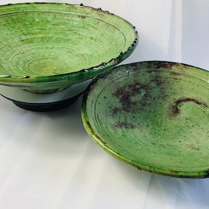 Peut inclure: Deux bols en céramique ronds et peu profonds avec une glaçure vert vif. Les bols présentent une surface texturée et marbrée avec des accents vert foncé et marron. Les bords ont un détail de rebord surélevé et irrégulier avec des picots.