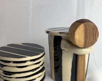 Un posavasos de cerámica hecho a mano con estampado de rayas negras y crema y acabado esmaltado brillante.