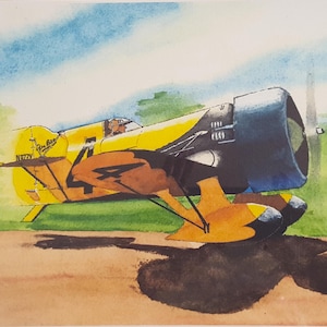 May include: Watercolor painting of a vintage yellow and brown airplane with a black engine and propeller. The plane is on a brown surface with a green and blue background. The plane has the text "N772Y" on the side.