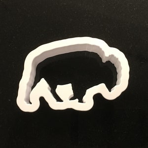 May include: White plastic cookie cutter shaped like a bison, a large, shaggy, wild mammal.