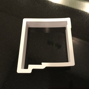 May include: White plastic cookie cutter shaped like the state of New Mexico.