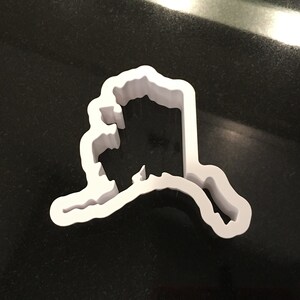 May include: White plastic cookie cutter shaped like the state of Alaska.