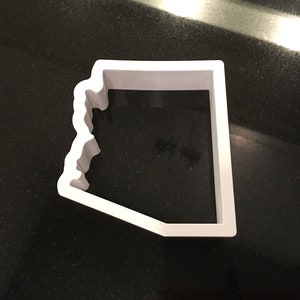 May include: A white plastic cookie cutter shaped like the state of Arizona.