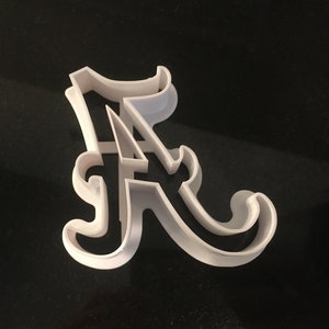 May include: White plastic cookie cutter shaped like the letter A. The letter is in a stylized font with a flourish at the top and bottom.