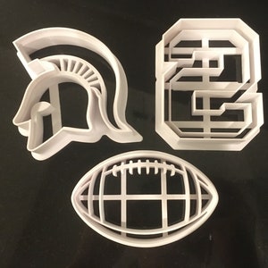 May include: Three white plastic cookie cutters: a football, a Spartan helmet, and the letter 'S'.