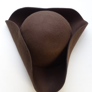 Peut inclure: Un chapeau tricorne en feutre marron avec une large bordure et une couronne arrondie.