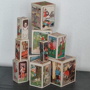 Può includere: Una collezione di blocchi di legno vintage, ogni lato con un'illustrazione colorata diversa. I blocchi sono impilati, mostrando varie scene e personaggi. Le illustrazioni sembrano provenire da un libro di fiabe per bambini.