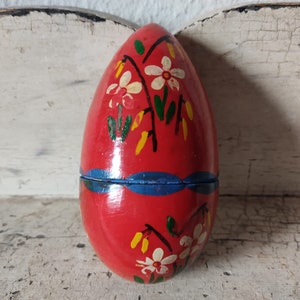Könnte beinhalten: Ein rotes Holzei mit einem blauen Band und weißen Blumen, die darauf gemalt sind. Das Ei ist eine Schachtel mit Scharnieren.