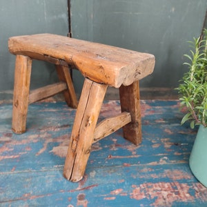 Könnte beinhalten: Ein rustikaler Holzhocker mit schlichtem Design. Der Hocker ist aus Naturholz gefertigt und hat eine gewitterte Oberfläche. Es ist ein kleiner Hocker, perfekt für einen kleinen Raum.