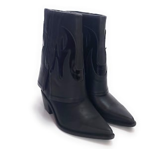 Puede incluir: Un par de botas vaqueras de cuero negro con un diseño de llama en el lateral. Las botas tienen una punta puntiaguda y un tacón bajo.