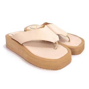 May include: A pair of beige platform sandals with a thick, textured sole. The sandals have a simple design with a single strap across the top of the foot.