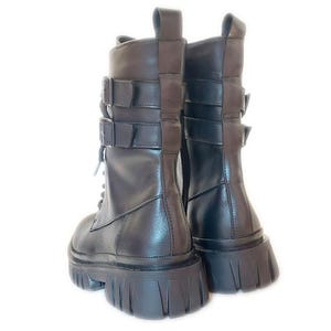 K&ouml;nnte beinhalten: Ein Paar schwarze Leder-Combat-Stiefel mit klobiger Sohle. Die Stiefel verf&uuml;gen &uuml;ber drei Schnallenriemen und ein Schn&uuml;rdesign. Die Stiefel haben eine Zuglasche oben und sind vor einem wei&szlig;en Hintergrund platziert.