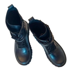 K&ouml;nnte beinhalten: Ein Paar schwarze Leder-Kampfstiefel. Die Stiefel haben ein Schn&uuml;rdesign, einen seitlichen Rei&szlig;verschluss und eine runde Spitze. Die Sohlen sind dick und die Stiefel haben einen kurzen Schaft. Die Stiefel sind vor wei&szlig;em Hintergrund.