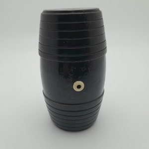 May include: A black wooden barrel with a small white circle on the side. The barrel has a textured surface and is approximately 10 cm tall.