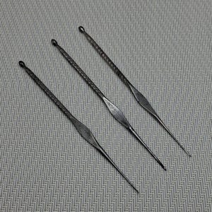 May include: Three antique metal tools with pointed ends and textured handles. The tools are arranged diagonally on a patterned surface. The metal has a dark, aged appearance, suggesting they are vintage or handcrafted.