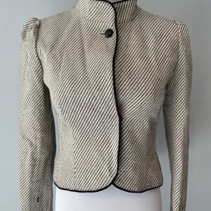 May include: A white and black striped blazer with a black trim and a single black button. The blazer has a mandarin collar and long sleeves.