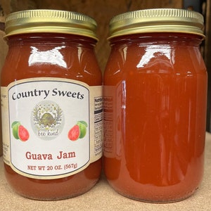 May include: Two glass jars of guava jam, labeled "Country Sweets" with a bee logo and the text "bee kind". The jars are filled with a bright red guava jam and have gold lids. The label also says "Guava Jam" and "NET WT 20 OZ. (567g)".