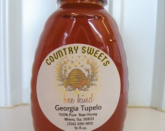 May include: A glass bottle of Georgia Tupelo honey with a red lid and a white label that says "COUNTRY SWEETS bee kind Georgia Tupelo 100% Pure Raw Honey Wrens, Ga. 30833 (706) 699-1810 16 fl oz."