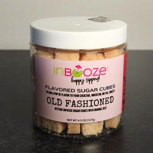 May include: A clear plastic jar filled with beige sugar cubes. The jar has a white lid and a pink label with the text "InBoze happy sipping!" and "Old Fashioned" in bold letters. The label also states the net weight is 4.5 oz (127g).