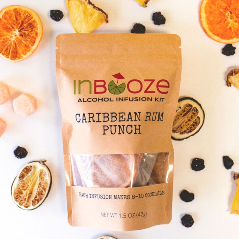 May include: A brown paper pouch with a clear window showing a brown powder inside. The pouch has the text "InBooze Alcohol Infusion Kit Caribbean Rum Punch" and "Each infusion makes 8-10 cocktails" printed on it. The pouch is surrounded by dried fruit slices, berries, and citrus fruits.