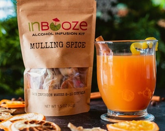 May include: A brown paper bag of "InBooze" alcohol infusion kit, "Mulling Spice", with a clear window showing the contents. A glass of orange-colored cocktail with a cinnamon stick and lemon peel garnish sits next to the bag. Dried orange slices are scattered around.