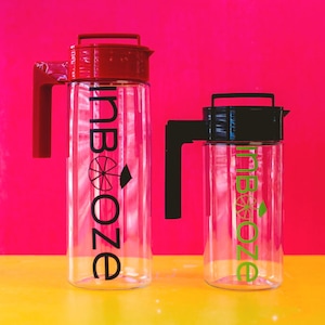 May include: Two clear glass pitchers with lids, one red and one black, both with the word "inBooze" printed on them. The pitchers are on a yellow surface.